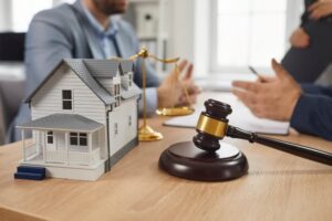 A group of people gathered around an office table, discussing matters with a gavel and a model of a house prominently displayed. The scene highlights concepts of real estate, property law, and legal services.