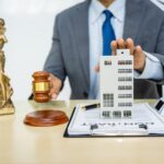 A land use lawyer in a formal suit works at his desk, focusing on contracts, legal matters, and urban planning issues such as building models, zoning, ordinances, and municipal regulations.