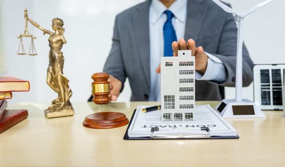 A land use lawyer in a formal suit works at his desk, focusing on contracts, legal matters, and urban planning issues such as building models, zoning, ordinances, and municipal regulations.
