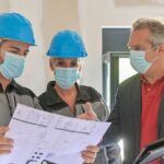 General and subcontractor meeting on a construction site between the architect and the craftsmen who wear a protective mask