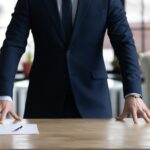 Company executive, CEO, owner in formal suit standing at work desk.