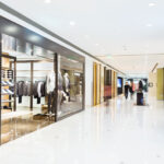 Indoor shopping mall corridor with retail store displays on both sides, showcasing clothing.