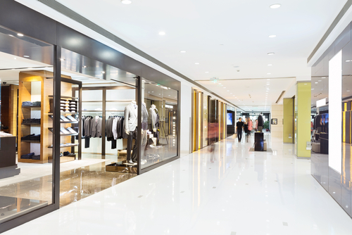 Indoor shopping mall corridor with retail store displays on both sides, showcasing clothing.